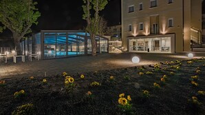 Un edificio moderno con estructura de vidrio y zona de piscina, rodeado por un jardín ajardinado con flores amarillas.