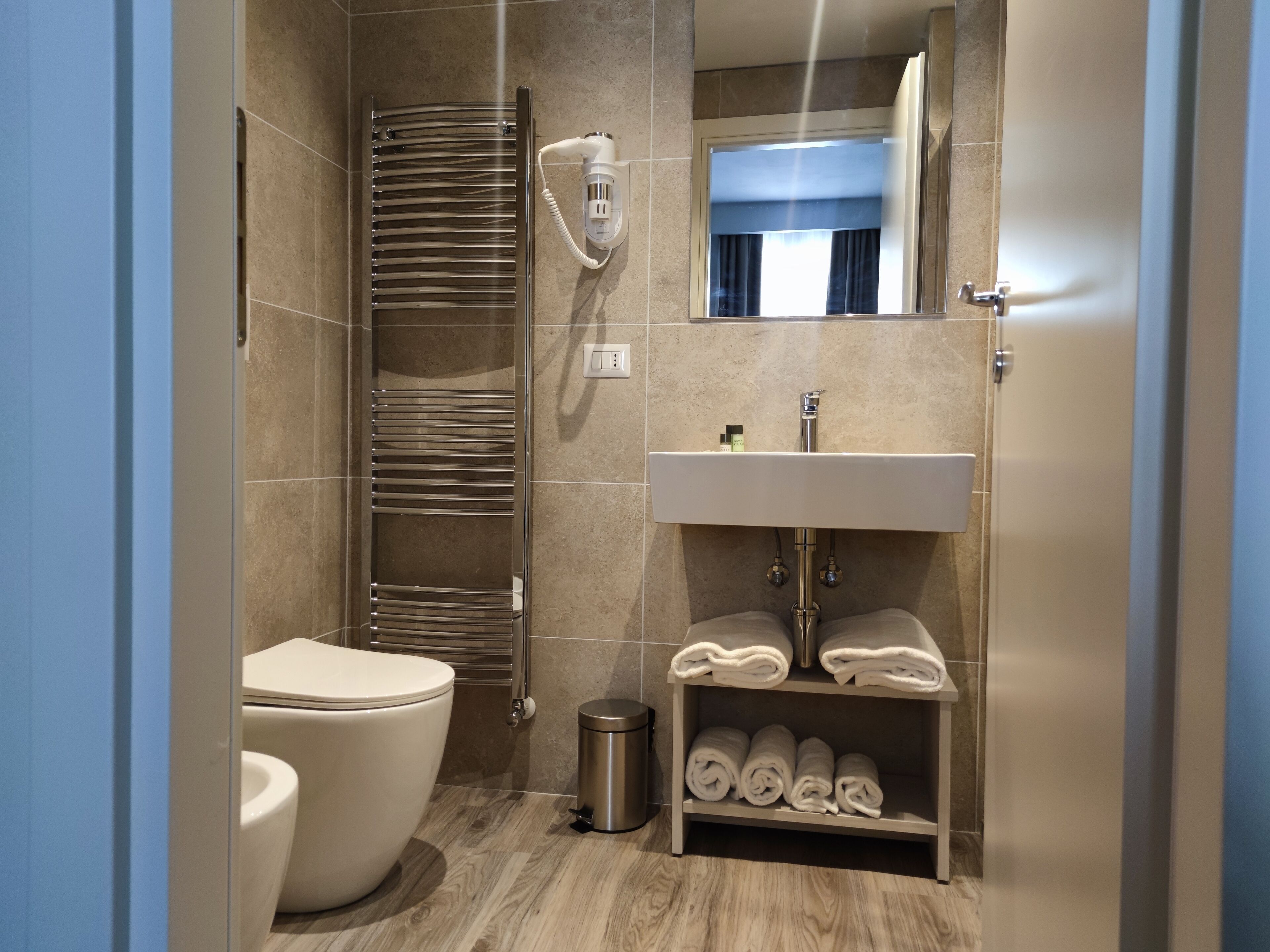 A modern bathroom with a toilet, a towel rack, a sink, and a mirror.