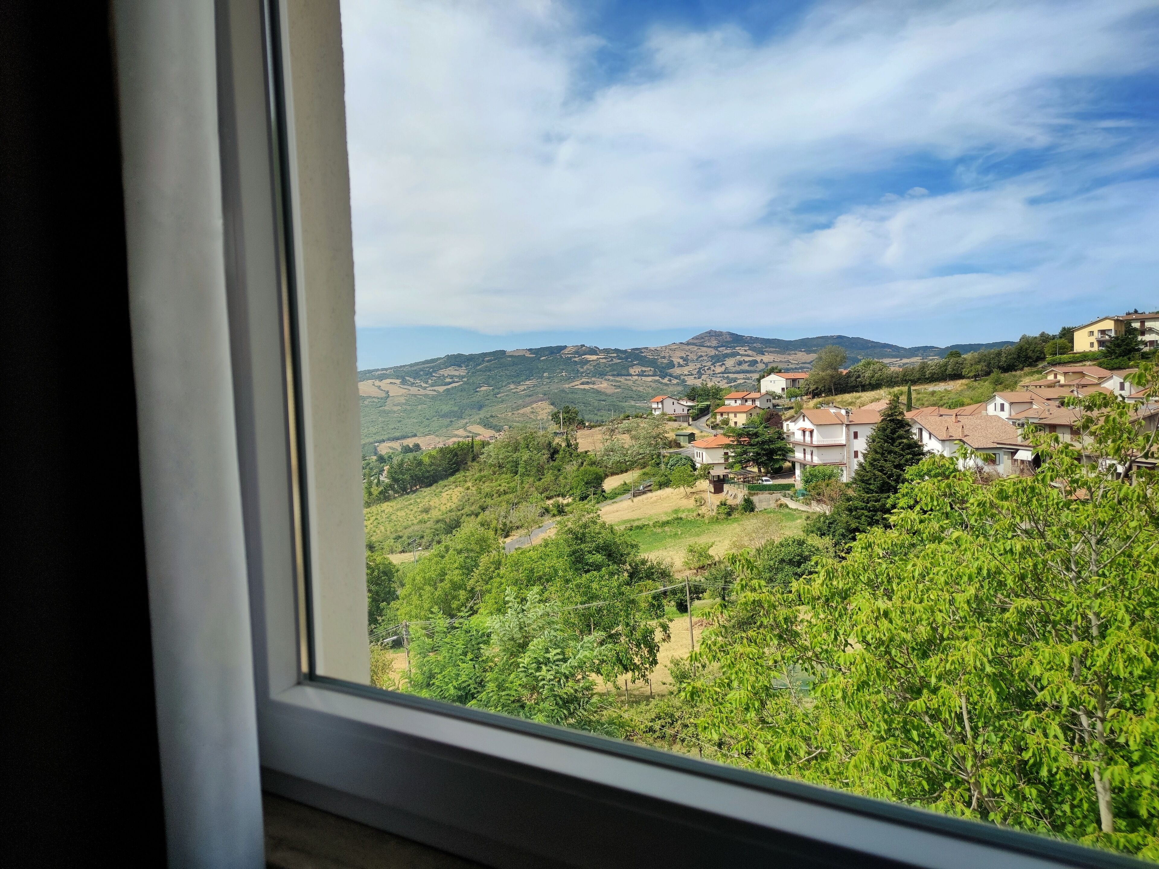 Una vista attraverso una finestra su un borgo collinare con case e vegetazione.