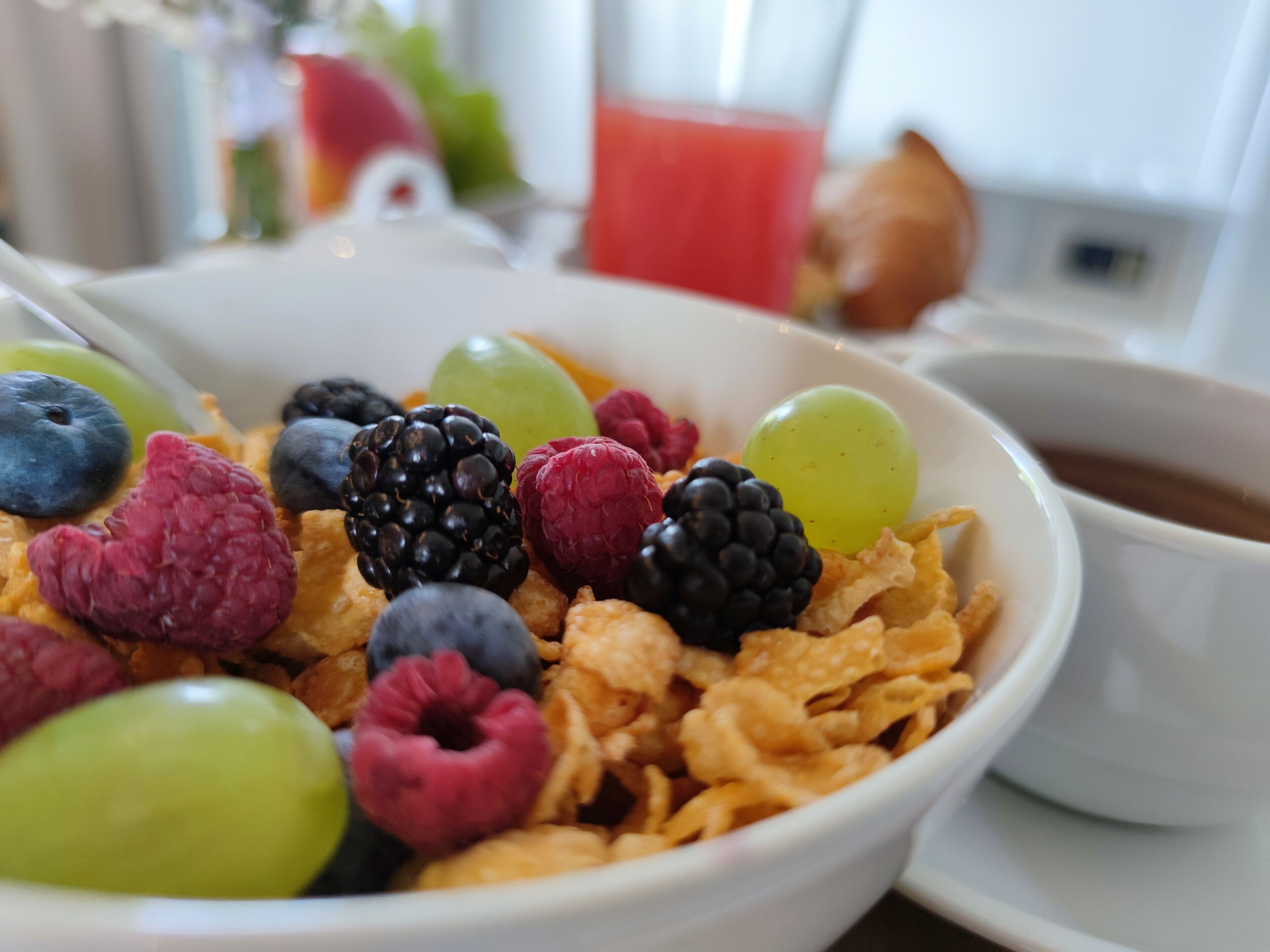 A bowl of cereal with various fruits and a glass of orange juice.