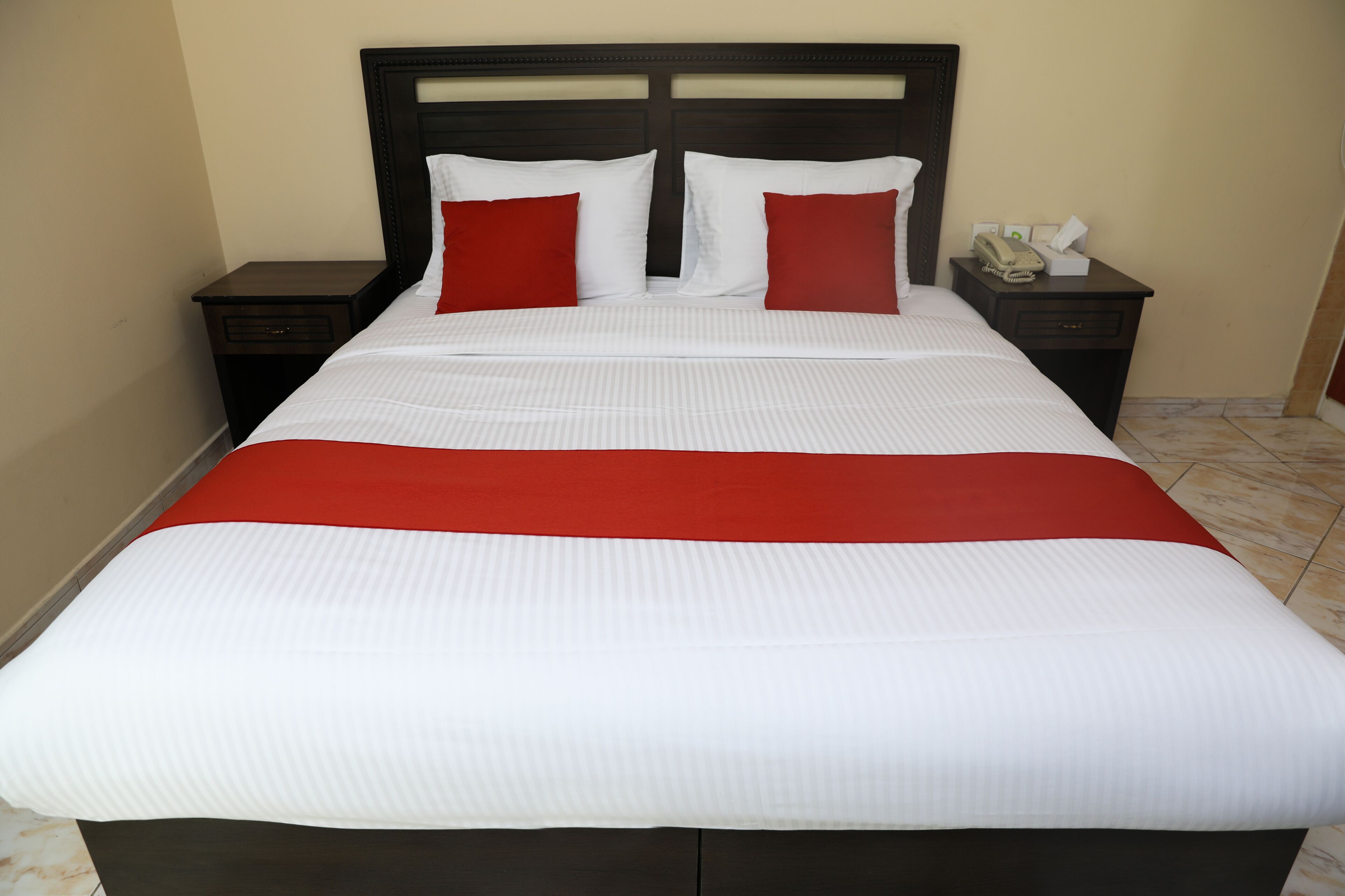 A neatly made bed with a white and red bedspread, two red pillows, and a wooden headboard.