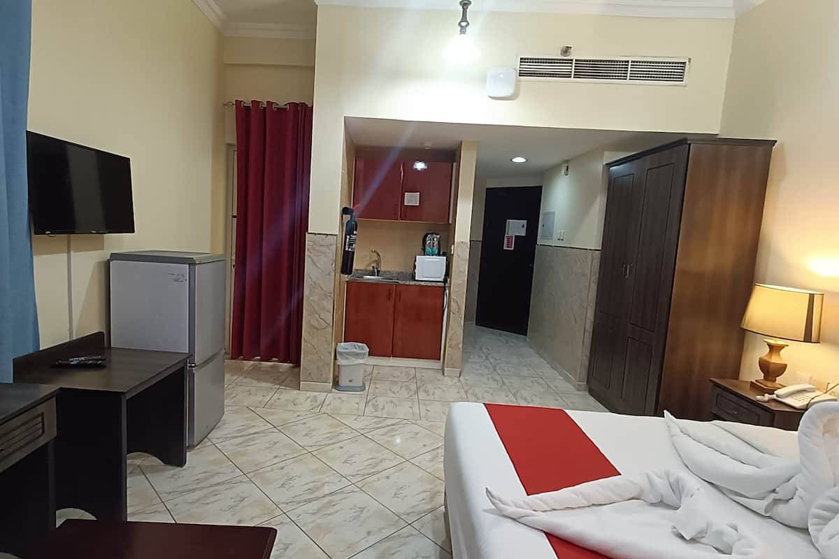 A hotel room with a bed, a desk, a television, a kitchenette, and a bathroom.