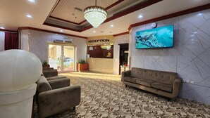 A reception area with a chandelier, a TV mounted on the wall, a reception desk, and a patterned carpet. - RUWI BEACH HOTEL APARTMENTS (Sharjah)