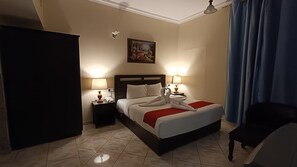 A hotel room with a bed, two bedside lamps, a painting on the wall, and a window with curtains.