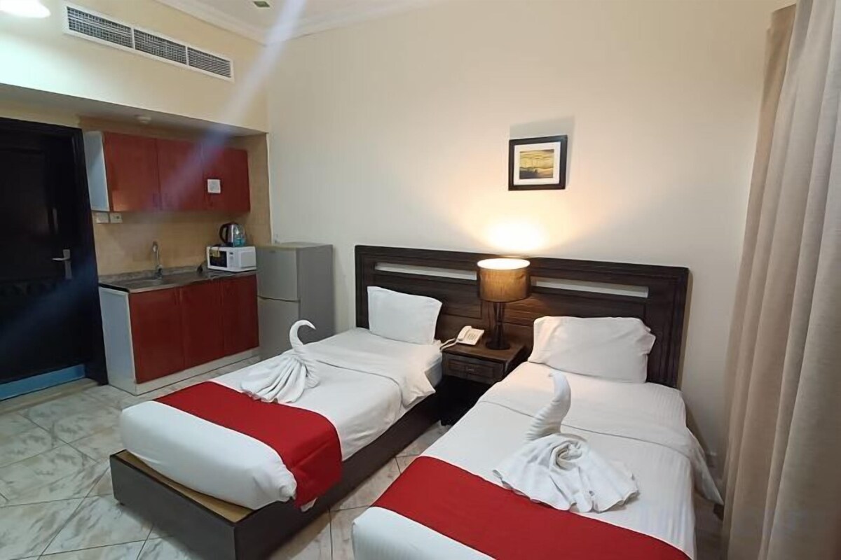 Quarto de hotel com duas camas, um kitchenette e uma luminária de cabeceira.
