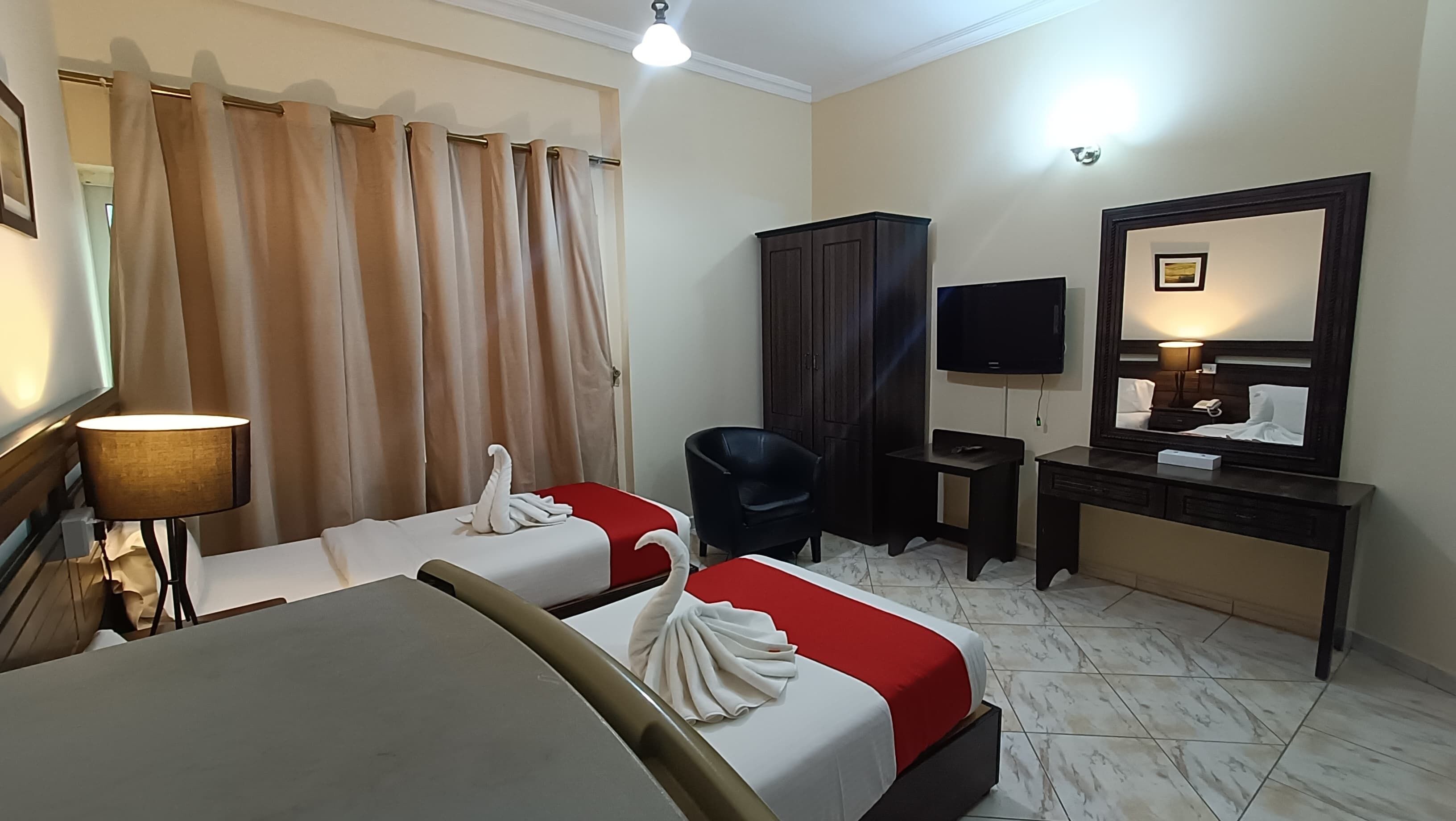 A hotel room with two beds, a desk, a chair, a TV, a wardrobe, and a mirror.