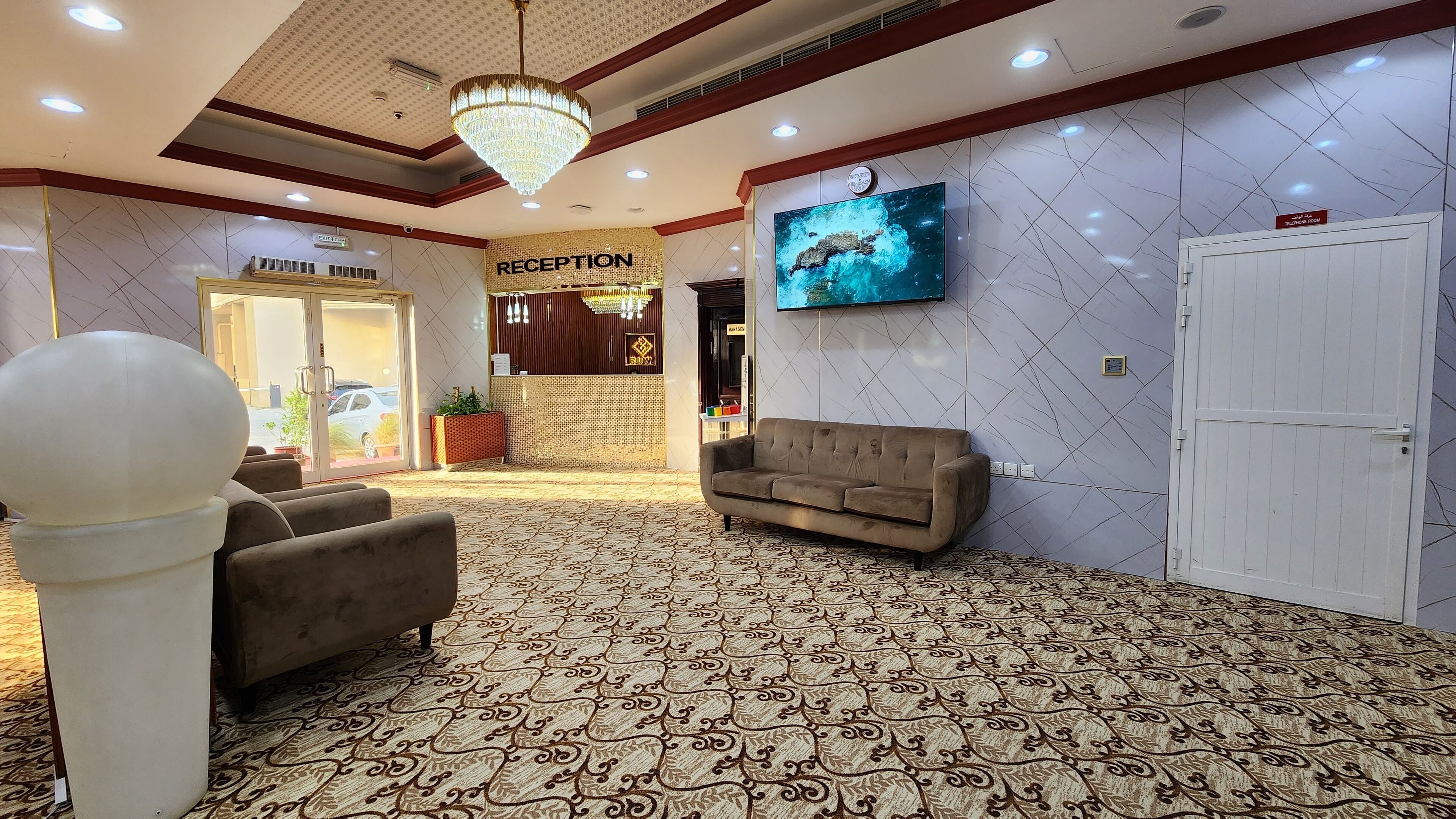 A reception area with a chandelier, a sofa, a television, and a reception desk.