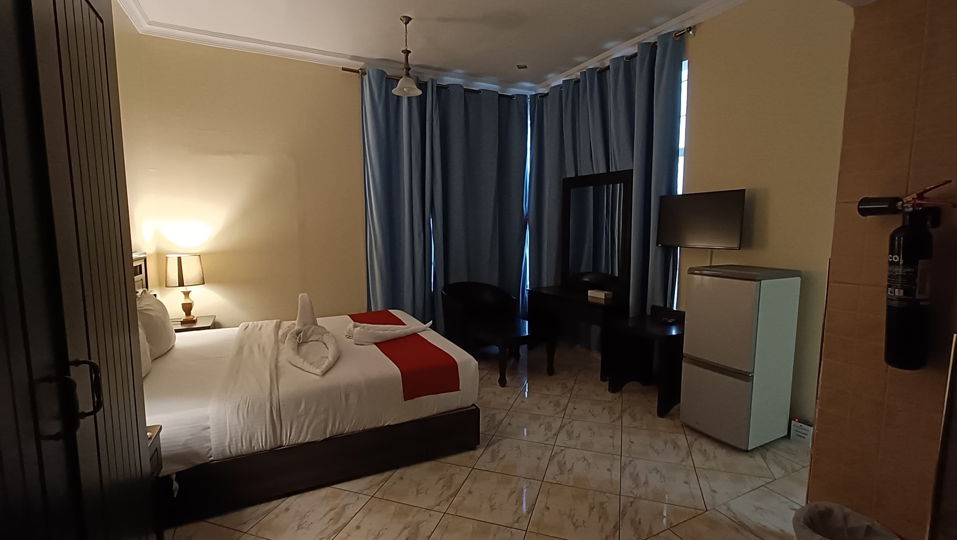 A hotel room with a bed, a desk, a chair, a TV, and a minibar.