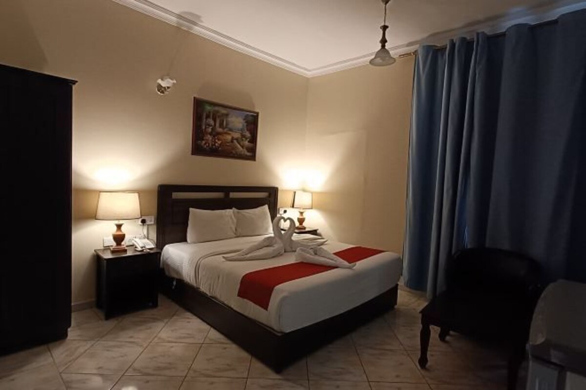 A hotel room with a bed, two bedside lamps, a painting on the wall, and a blue curtain.