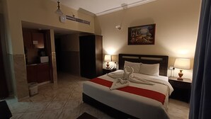 A hotel room with a large bed, two bedside lamps, a painting on the wall, and a bathroom visible through an open door. - RUWI BEACH HOTEL APARTMENTS (Sharjah)