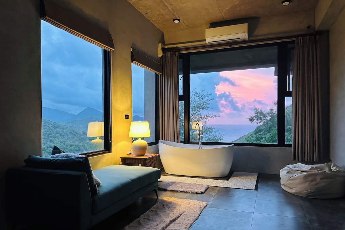 A modern bathroom with a bathtub, large windows, and a view of the mountains.
