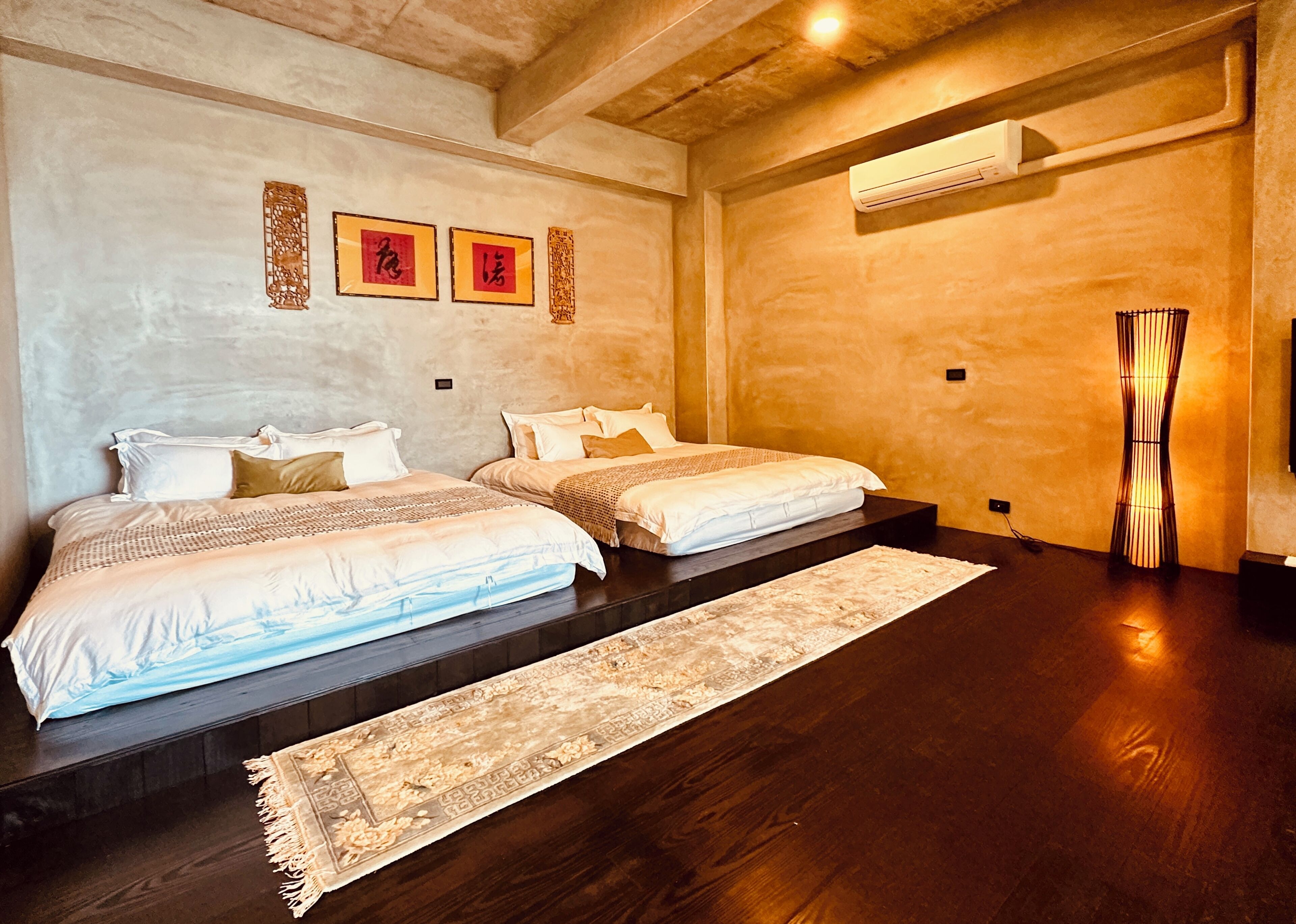 Un dormitorio con dos camas, piso de madera, alfombra grande y cuadros en la pared.