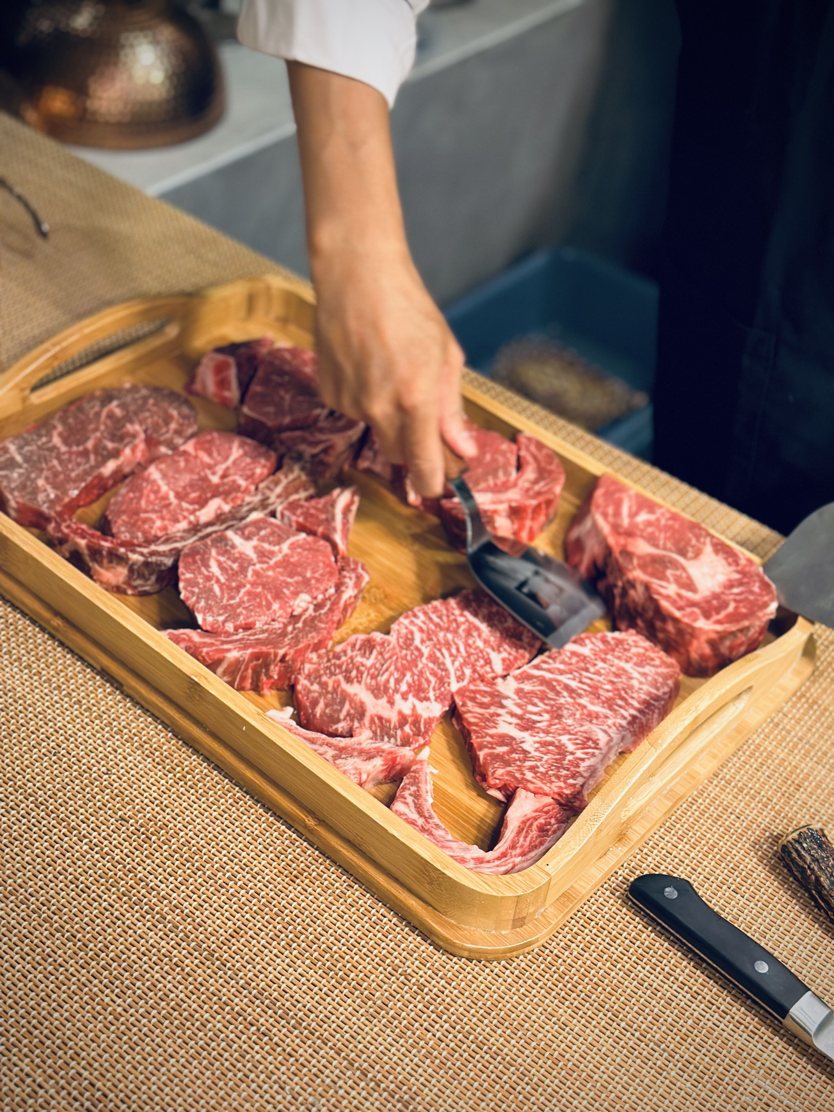 A person slicing raw beef on a wooden cutting board.
