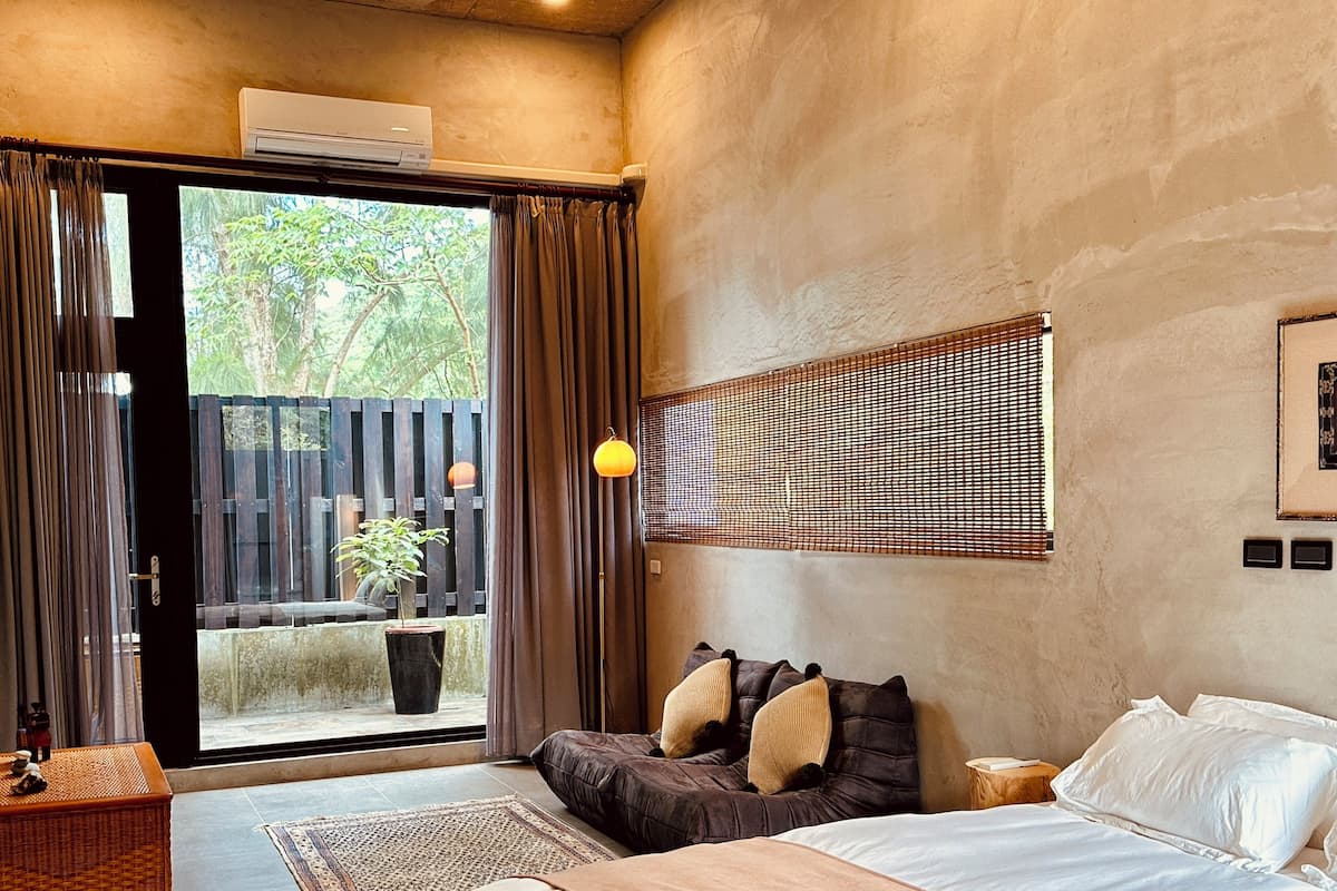 A bedroom with a bed, a large window, a potted plant, and a wall-mounted light fixture.