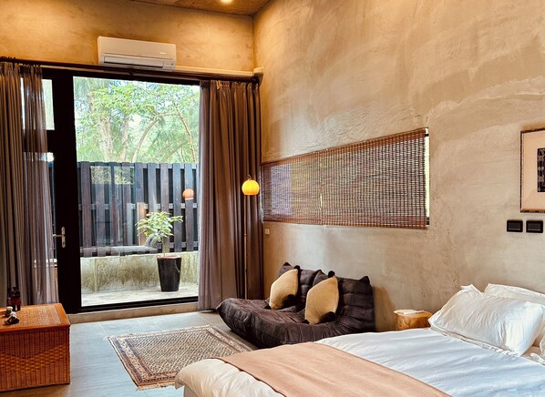 Een slaapkamer met een bed, een groot raam, een kamerplant en een wandlamp.