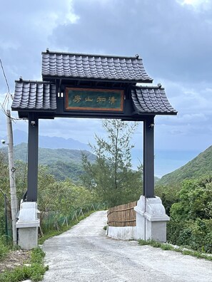 Een traditionele Chinese poort met een bordje, dat uitkomt op een pad omgeven door groen en bergen.