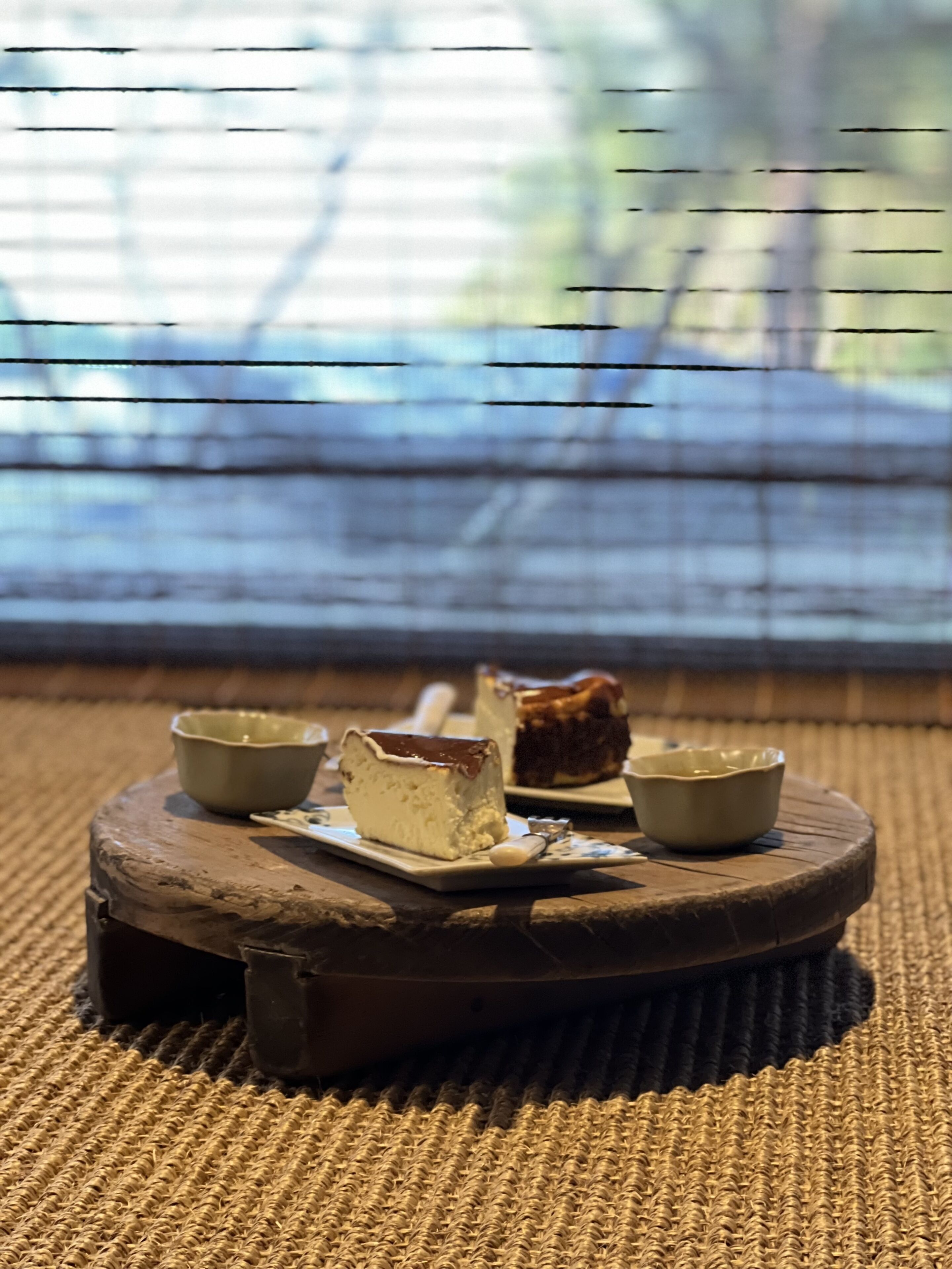 Una mesa redonda de madera con un tapete tejido, sosteniendo un pastel y dos tazones pequeños.
