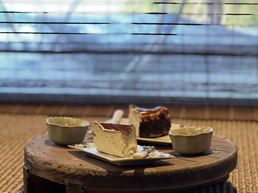 Una mesa redonda de madera con un tapete tejido, sosteniendo un pastel y dos tazones pequeños.