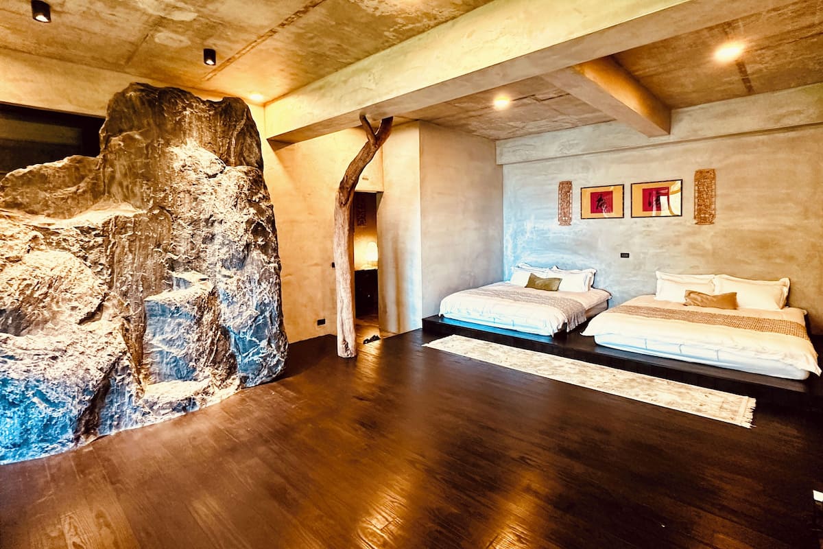 A bedroom with a large rock feature, wooden flooring, and a bed with white bedding.
