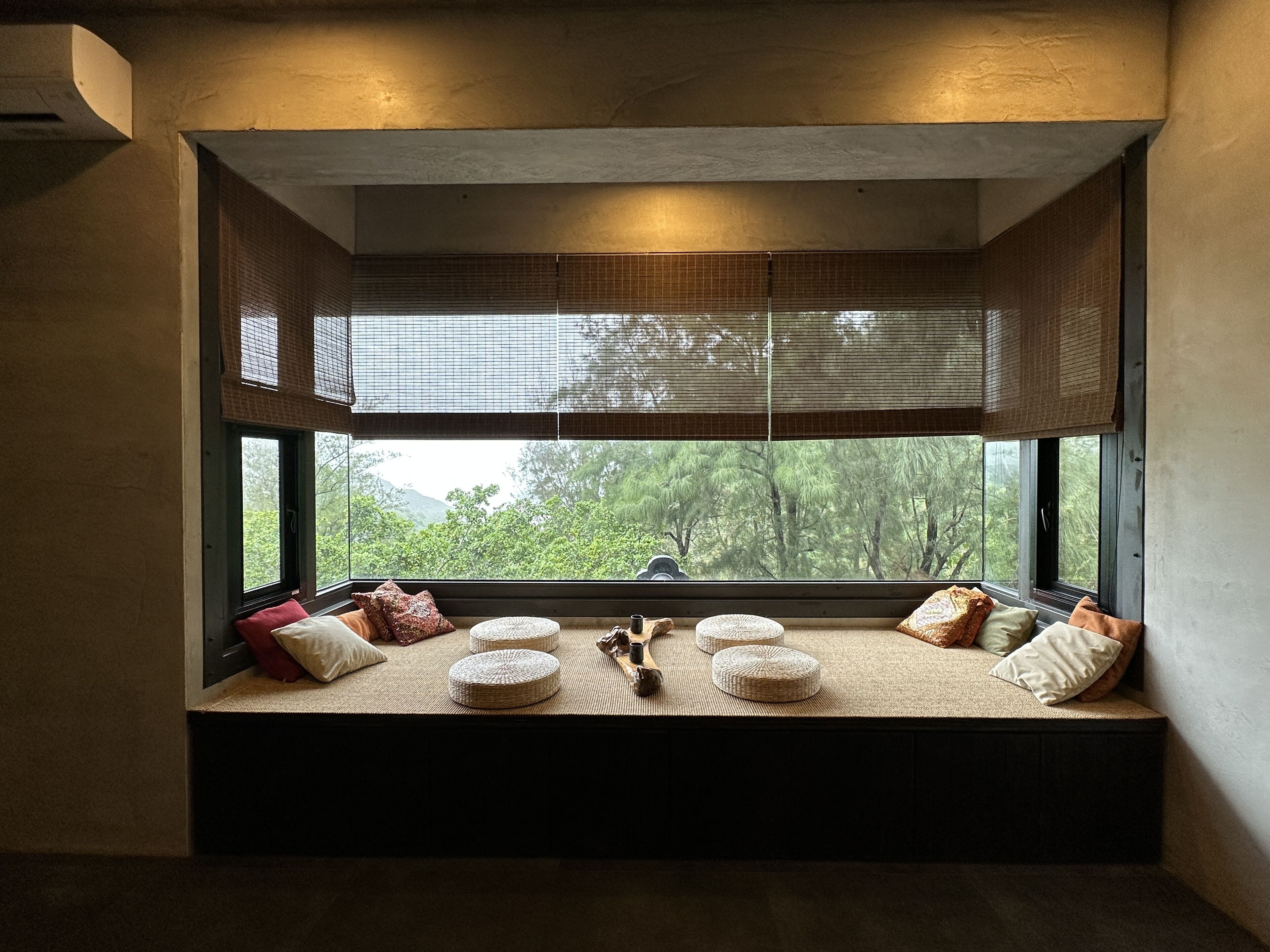A cozy reading nook with a large window, cushioned seating, and a small table with a decorative item.