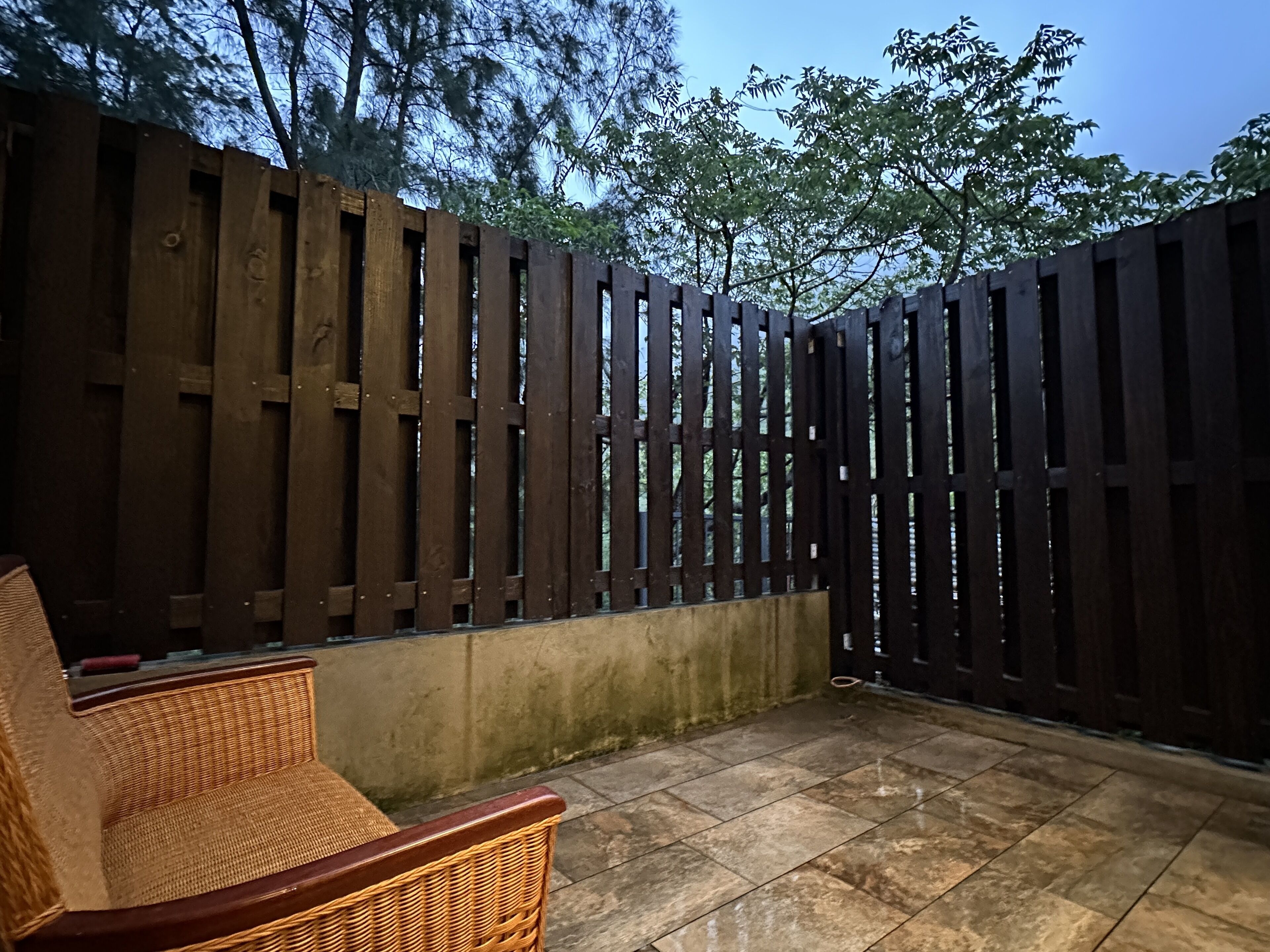 A patio area with a wicker chair, a tiled floor, and a wooden fence.