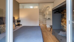 Ein modernes Schlafzimmer mit Bett, Nachttisch, Lampe und einem Kleiderschrank mit Kleiderstange.