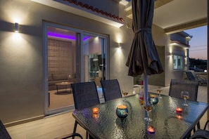 A modern outdoor dining area with a glass table, chairs, and candles.