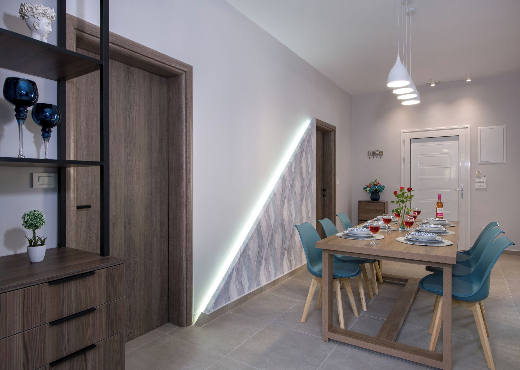A modern dining area with a wooden table, blue chairs, and a built-in shelf with decorative items.