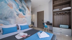 Una habitación de hotel moderna con un cuadro abstracto grande, una cama con ropa de cama azul, un escritorio con una computadora portátil y un vestidor.