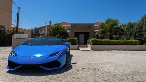 Un coche deportivo azul aparcado frente a un edificio con tejado de tejas rojas y entrada de grava.