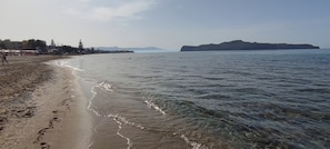 A beach with clear water, a sandy shore, and a distant mountain.
