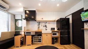 A compact kitchen with a microwave, stove, and black refrigerator. There is a wooden bench and a small dining table. - Ikebukuro, cafe style, 2LDK, detached house, 2 shower rooms, 2 toilets (豊島区)