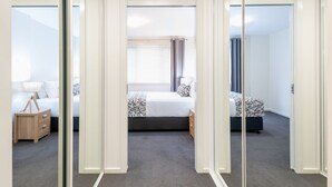 Habitació d'hotel amb llit, taula de nit, làmpada i vista a través d'una porta de vidre.
