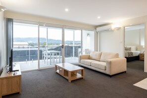 A modern living room with a sofa, a coffee table, and a TV on a wooden stand. - Warners Bay Apartments (Warners Bay)