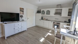 Uma cozinha moderna com armários brancos, uma televisão de tela plana e uma área de refeições com mesa e cadeiras.