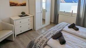 Quarto com uma cama, guarda-roupa, escrivaninha e janela com cortinas.