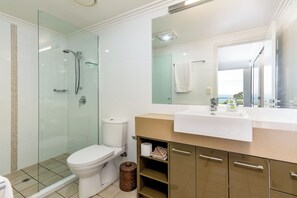 Features a glass-enclosed shower, white toilet, and large mirror.