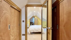 A bedroom with a bed, a wooden wardrobe, and a door leading to another room. - Little Vintners by inspirestays.com - a cottage that sleeps 2 guests in 1 bedroom (Gay Street, Pulborough)