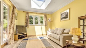 A living room with a sofa, a TV, a lamp, and a window with curtains. - Little Vintners by inspirestays.com - a cottage that sleeps 2 guests in 1 bedroom (Gay Street, Pulborough)