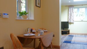 A dining area with a table set for two, chairs, a potted plant, and a window with curtains. - Little Vintners by inspirestays.com - a cottage that sleeps 2 guests in 1 bedroom (Gay Street, Pulborough)