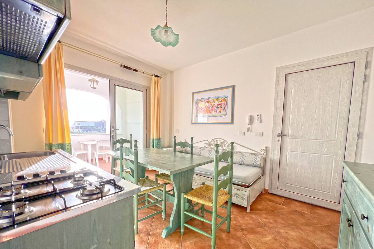 A kitchen with a gas stove, a dining table with chairs, a bench, and a door.