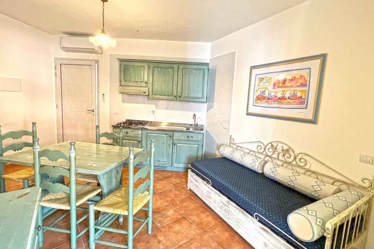 A compact kitchen with green cabinets, a dining table with chairs, and a sofa with patterned cushions.
