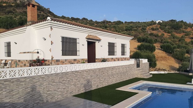 Una casa moderna con piscina, fachada blanca y un muro de piedra.