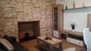 Una sala de estar con pared de ladrillo, chimenea, aparador de madera con puertas de cristal, sofá, mesa de centro y una planta.