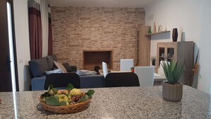 Una sala de estar con pared de piedra, un sofá, una mesa de comedor con una cesta de frutas y una planta en maceta.