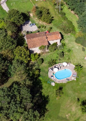 An aerial view of a property with a swimming pool, stone patio, and a house with a tiled roof.