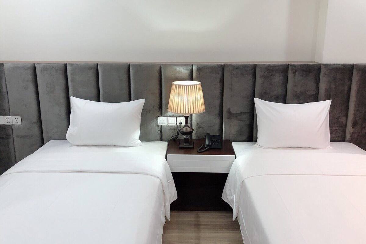 A hotel room with two beds, a nightstand with a lamp, and a telephone.