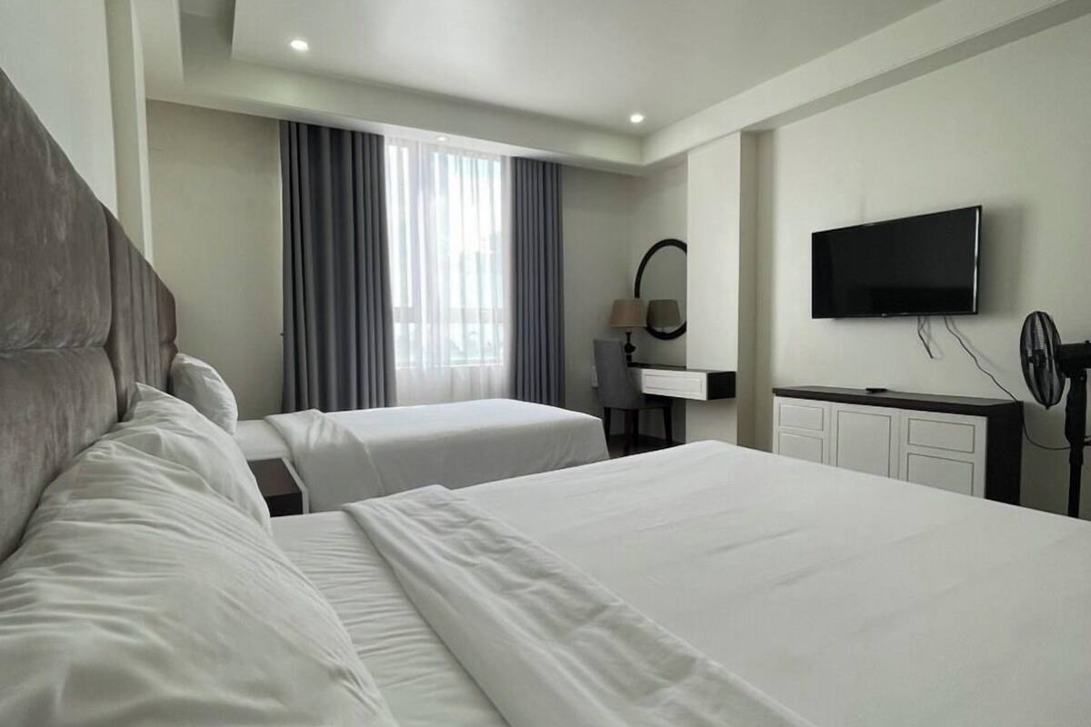 A hotel room with two beds, a desk, a chair, a TV, and a window with curtains.