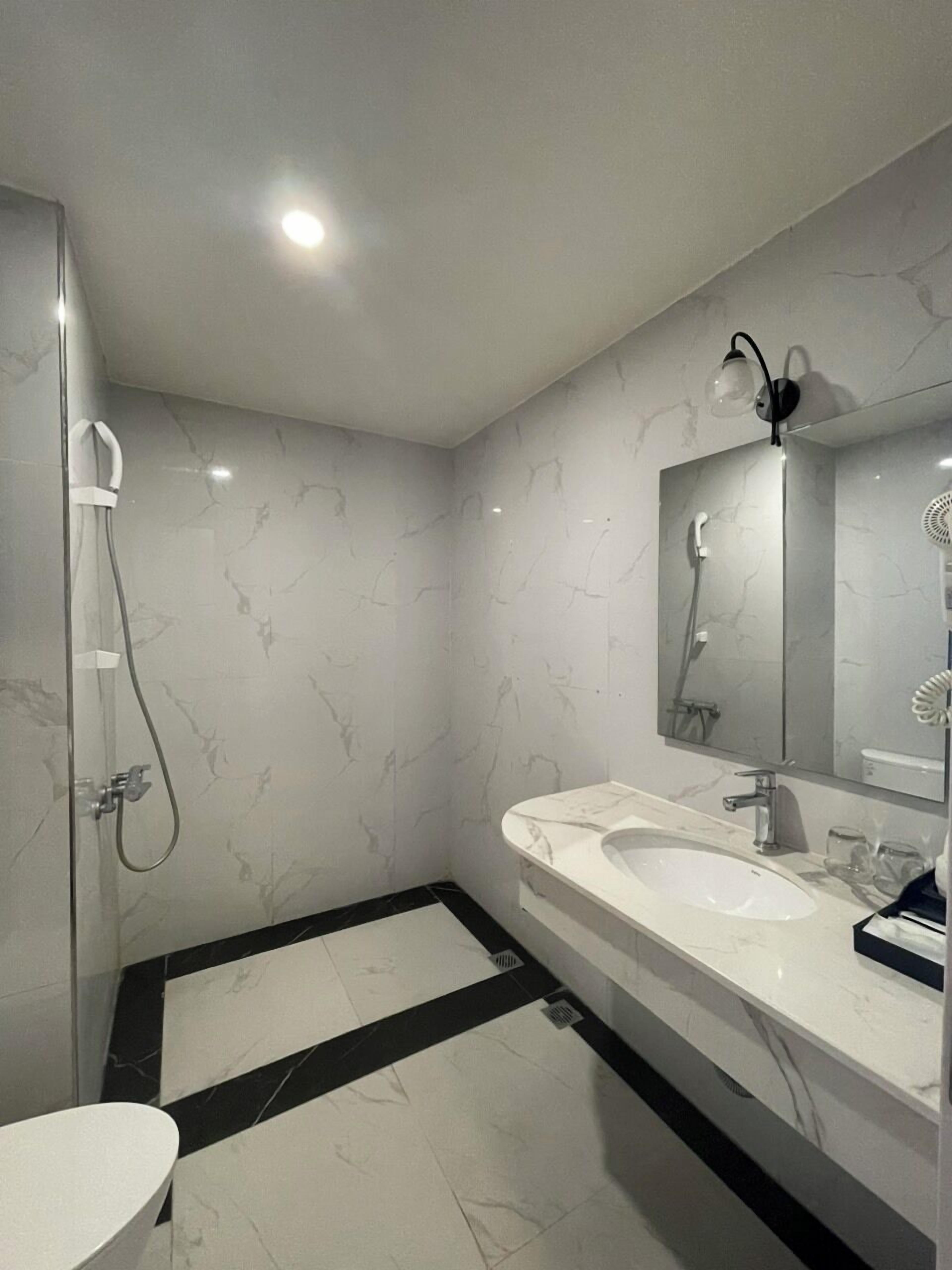 Une salle de bain moderne avec une douche à parois de verre, deux vasques, un grand miroir et un sol carrelé en noir et blanc.