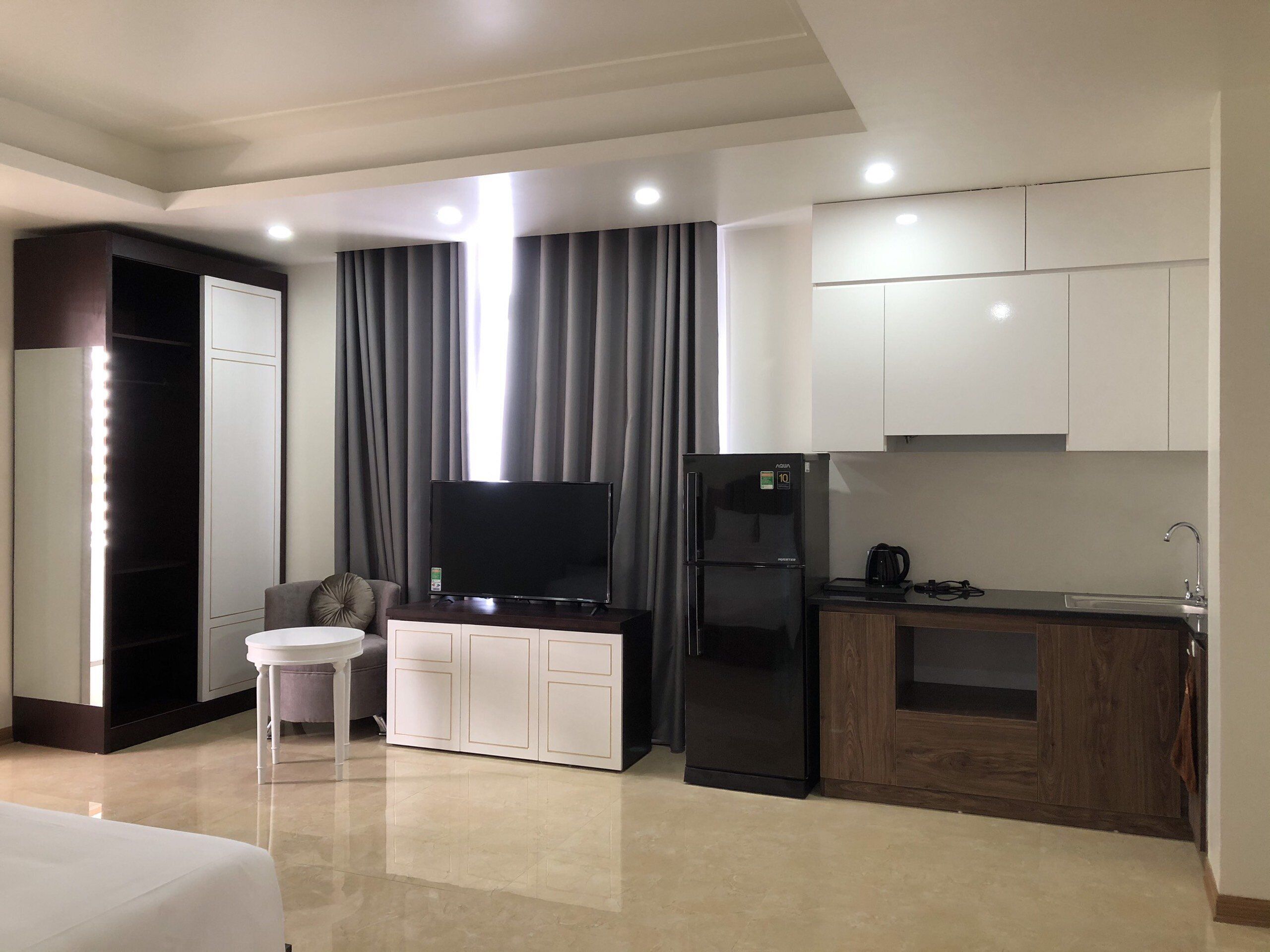 Una habitación de hotel moderna con televisor de pantalla plana, refrigerador, kitchenette y tocador con espejo.